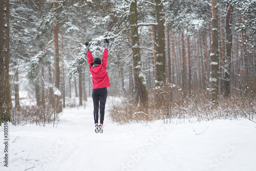 Winter run. Workout. Young sporty woman jumping in winter forest.