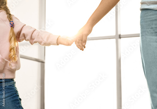 Mother holding hands with her child indoors, closeup. Happy family