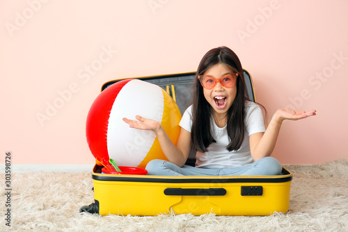 Happy girl with suitcase and inflatable ball near color wall