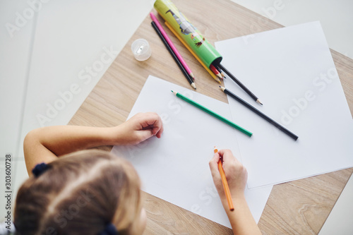 Top view of little girl with pencils and empty paper sheet on the table