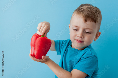 Little kid holding pepper in his hands on blue background. Vegan and healthy concept
