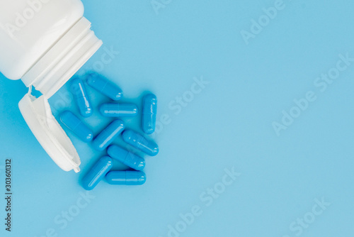 Blue capsules, pills on a blue background. Capsules in a white jar. Vitamins, nutritional supplements for women's health