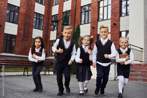 Group of kids in school uniform posing to the camera outdoors together near education building