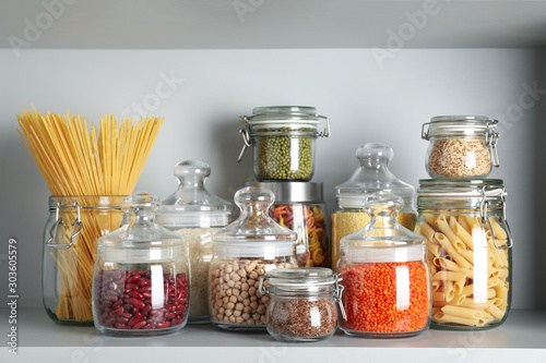 Glass jars with different types of groats and pasta on white shelf photo