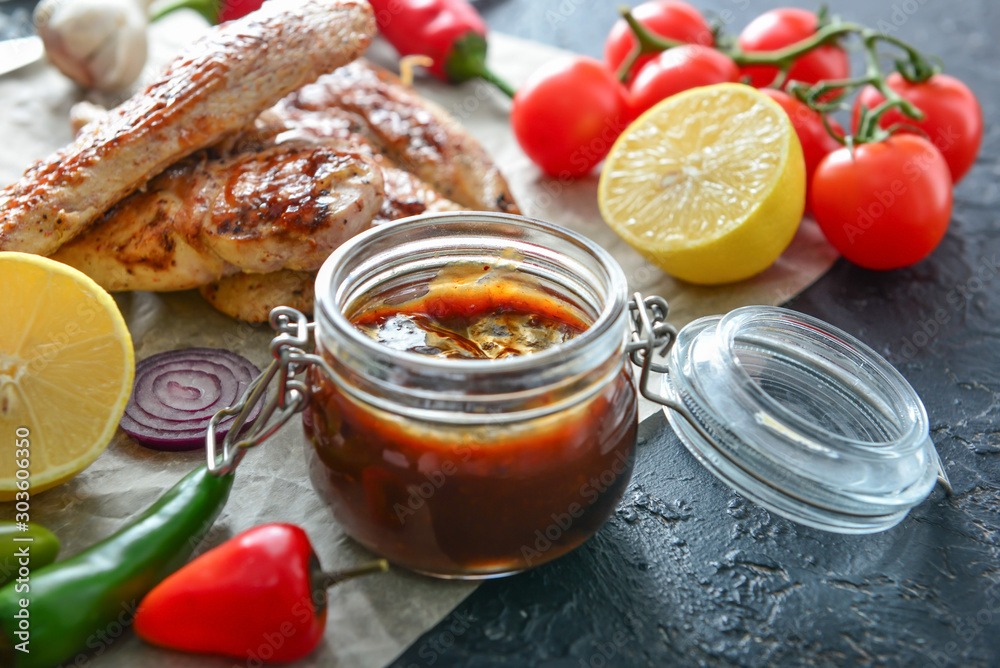Jar of tasty barbecue sauce, chicken, vegetables and spices on table Jar of tasty barbecue sauce, chicken, vegetables and spices on table