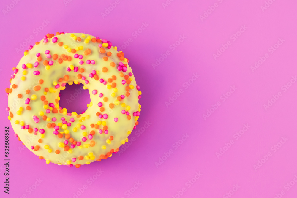 Icing donut on a pink background with text space. Flat lay, purple mockup, template. Yellow donut with multicolored sprinkles. Unhealthy high-calorie food. Icing donut on a pink background with text space. Flat lay, purple mockup, template. Yellow donut with multicolored sprinkles. Unhealthy high-calorie food.