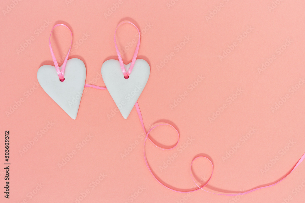 Love for Valentine's day - Hearts hung together on pink ribbon. Pastel color paper background with copy space for text. Flat lay.