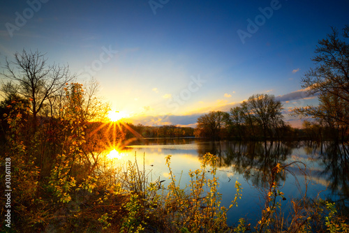 Long exposure sunset or sunrise over river side of Mississippi and the sun is reflex with water surface and distribution sun rays and small trees in foreground and clear blue sky