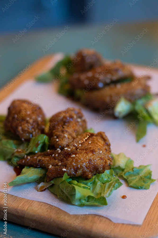 Korean fried chicken wings with sweet spicy soy sauce and sesame and lettuce on a wooden platter
