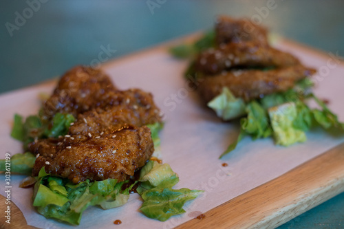 Korean fried chicken wings with sweet spicy soy sauce and sesame and lettuce on a wooden platter
