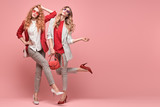 Fashionable woman with stylish hairstyle, makeup dance. Two Shapely blonde redhead girl having fun, trendy red outfit, heels, fashion hair, make up. Excited model, beauty dancing fun concept on pink
