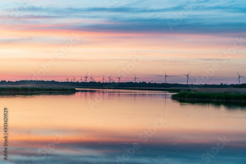 Evening sunlight on coast  pink and golden clouds and wind turbine. Sky reflection on water.  Wind generator for electricity  alternative energy source. Windmill for electric power production.