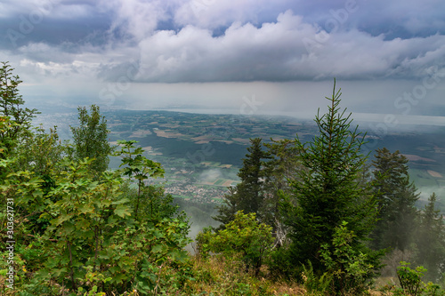 Top view of low dark clouds with falling rain in the distance,fog,lake and city buildings.Department Haute-Savoie in France.