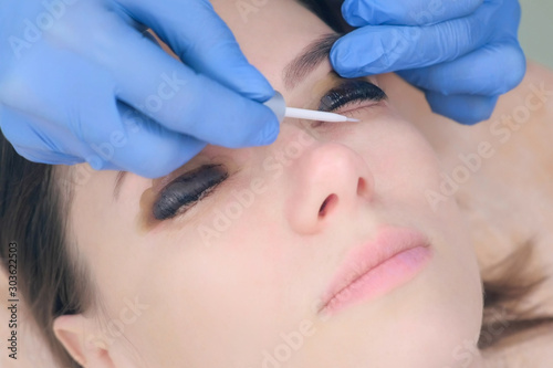 Beautician applying solution on lashes uses brush after lamination lift procedure in beauty salon, face closeup. Cosmetologist making lash lifting in cosmetology clinic.