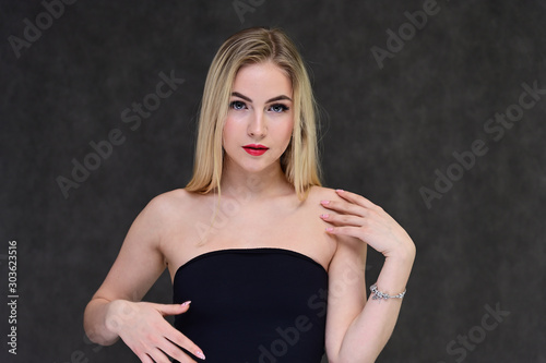 The concept of fashionable glamor, cosmetics and beauty with a pretty girl. Portrait of a fashionable beautiful blonde model with long hair, great makeup, on a gray background.