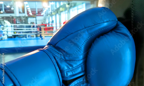A hand in a boxing glove hits a boxing bag against the background of a boxing ring in a fitness center