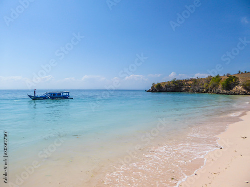 A peaceful Pink Beach in Lombok, Indonesia. Some boats are placed on the shore, others are drifting on a calm surface of the sea. Hidden gem of Indonesia, unspoiled place by humans. Relaxation
