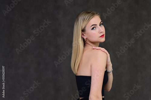 The concept of fashionable glamor, cosmetics and beauty with a pretty girl. Portrait of a fashionable beautiful blonde model with long hair, great makeup, on a gray background.