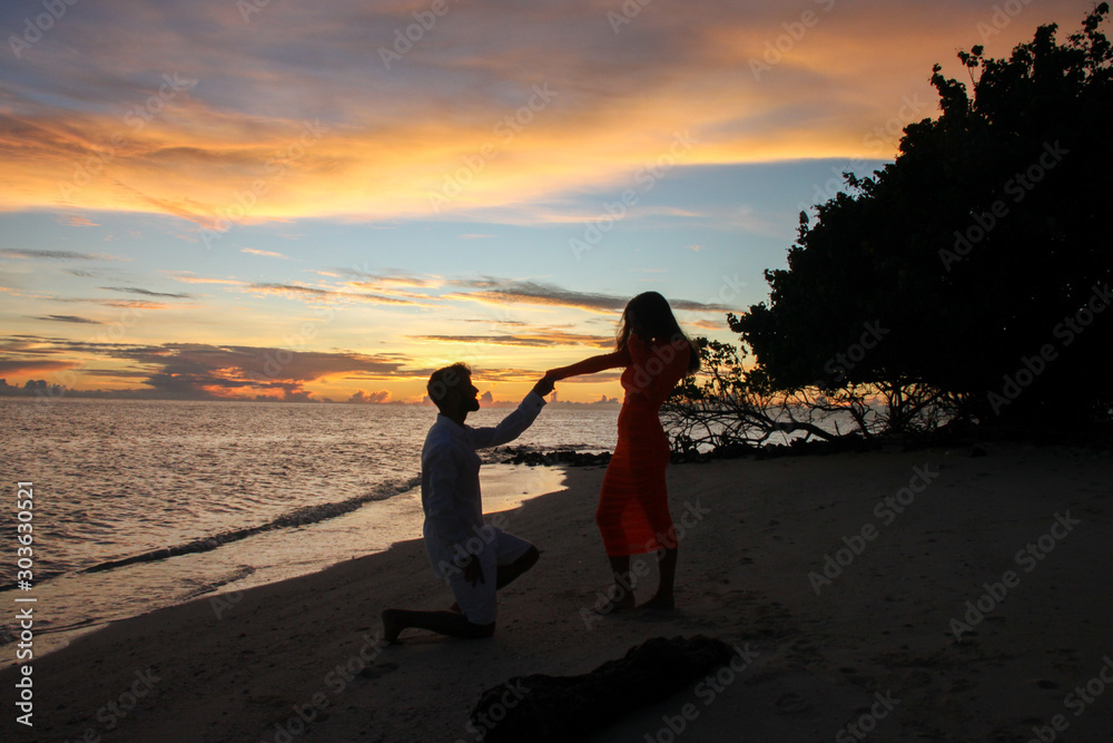 man dressed in white asking marriage to woman in red dress during sunset