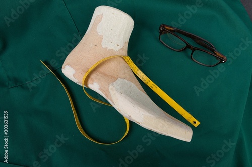 a wooden last on a green clobber with a measuring tape and glasses