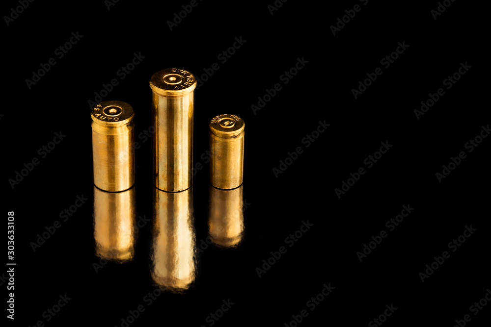 Comparison of sizes of different used bullet shells on a black isolated background with reflection from a tin table top. View of the different caliber cartridges. Comparison of sizes of different used bullet shells on a black isolated background with reflection from a tin table top. View of the different caliber cartridges.