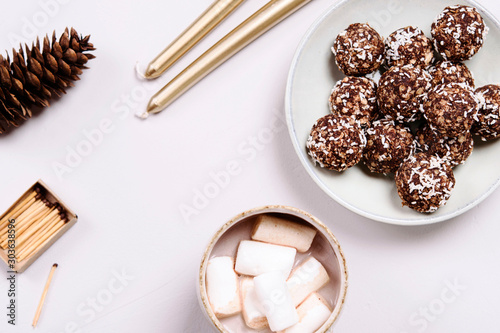 Swedish chocolate balls and cup of cocoa with marshmallow on grey concrete table. Cozy winter breakfast. Chokladbollar. Homemade healthy raw cocoa oatmeal balls sprinkled with coconut flakes