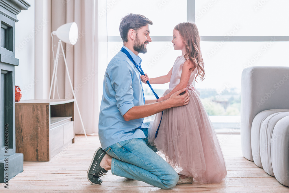 side view of daughter tying tie on her father standing face to face in living room side view of daughter tying tie on her father standing face to face in living room