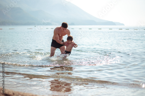 Young father and his little son play together in a water. Scenic sea and mountain view  summer time vacation