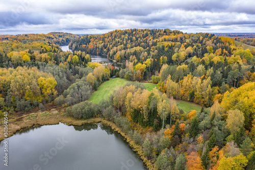 Forest in autumn colors. Colored trees and a meandering blue river. Red, yellow, orange, green deciduous trees in fall. Veclaicene, Latvia, Europe