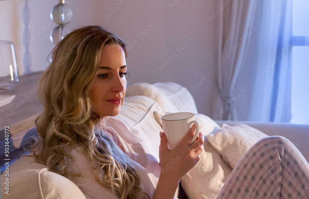 Blond mature woman sitting on the couch relaxes by drinking a cup of tea'