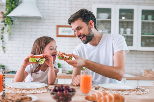 dad feeding girl eating with his sandwich for breakfast on the kitchen photo