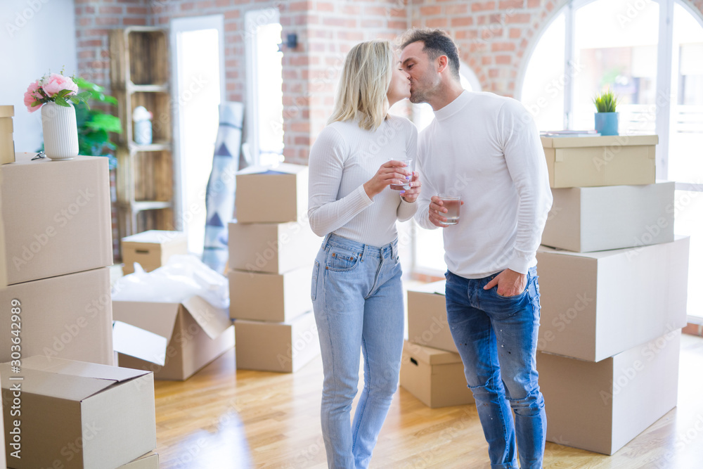 Young beautiful couple standing drinking cup of coffee and kissing at new home around cardboard boxes Young beautiful couple standing drinking cup of coffee and kissing at new home around cardboard boxes