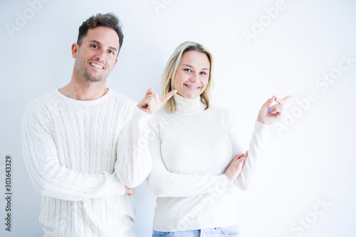 Young beautiful couple wearing casual t-shirt standing over isolated white background with a big smile on face, pointing with hand and finger to the side looking at the camera.