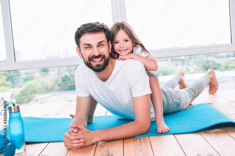 portrait of father and daughter lying on the yoga mat and smiling at the camera
