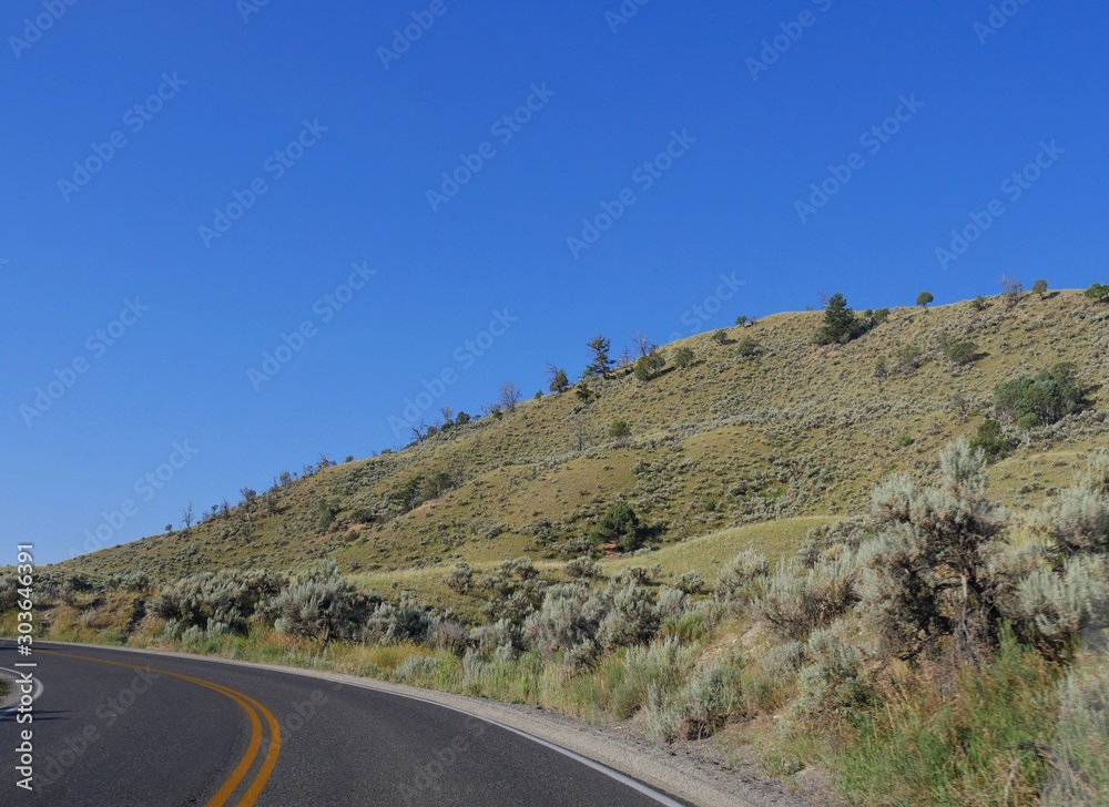 Sloping hills with sparse vegetation along a paved road at Yellowstone National Park heading toward Gardiner, Montana. Sloping hills with sparse vegetation along a paved road at Yellowstone National Park heading toward Gardiner, Montana.