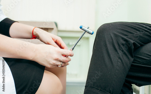 Neurologist checks reflexes hammering knee.  photo