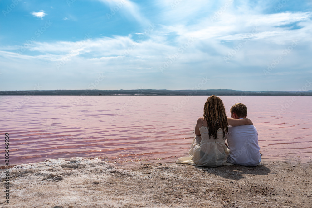 cute teenager brothers sitting on a shore of amazing pink lake
