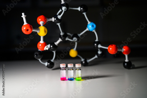 Three colourful solution in different LCMS glass vial on a white bench with molecular model background for biomedical research photo