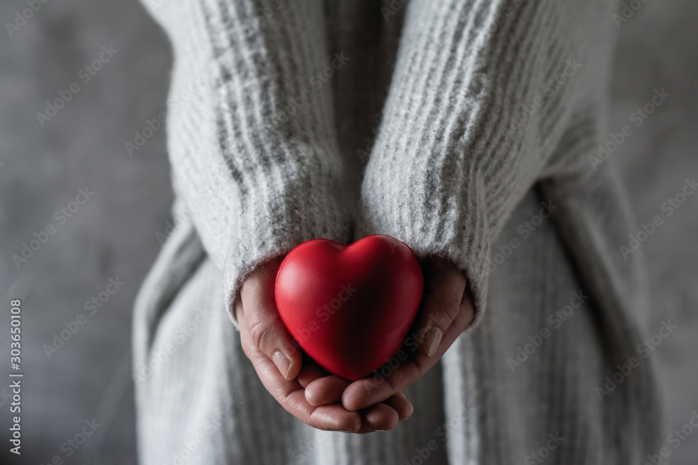 Girl in a knitted winter sweater holding a small red valentines heart. Concept Girl in a knitted winter sweater holding a small red valentines heart. Concept