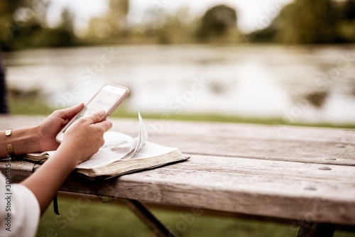 Closeup shot of a female using her smartphone with the bible on the table and blurred background photo