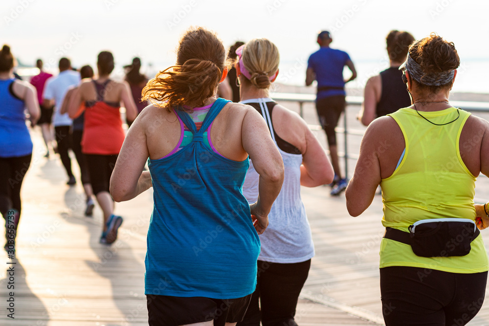 Obraz premium Rear view of runners in a race on a boardwalk by the beach