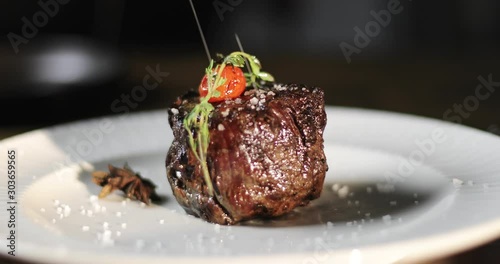 Cooks hand puts a fresh fried steak on white plate and maiking final decoration of dish. photo