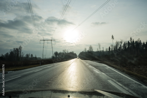 View of the asphalt road through the windshield of the car. Drive on the highway towards the sun. Autumn, evening, cloudy. © Viktor