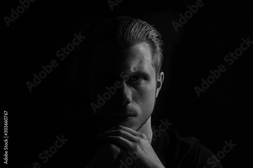 Black and white portrait of young serious looking man. Low key, dark background studio shot.