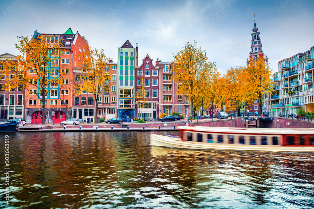 Stunning autumn cityscape of Amsterdam. Famous Dutch channels and excursion boat. Colorful morning landscape in Netherlands, Europe. Traveling concept background..