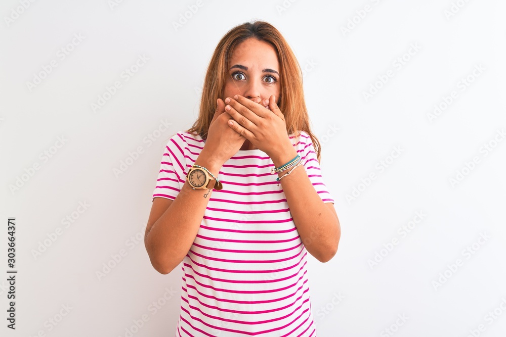 Young redhead woman wearing striped casual t-shirt stading over white isolated background shocked covering mouth with hands for mistake. Secret concept. Young redhead woman wearing striped casual t-shirt stading over white isolated background shocked covering mouth with hands for mistake. Secret concept.
