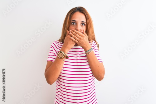 Young redhead woman wearing striped casual t-shirt stading over white isolated background shocked covering mouth with hands for mistake. Secret concept.