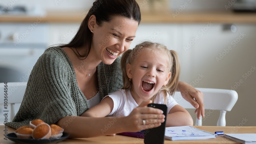 Smiling young mother showing funny cartoons to overjoyed daughter. Smiling young mother showing funny cartoons to overjoyed daughter.