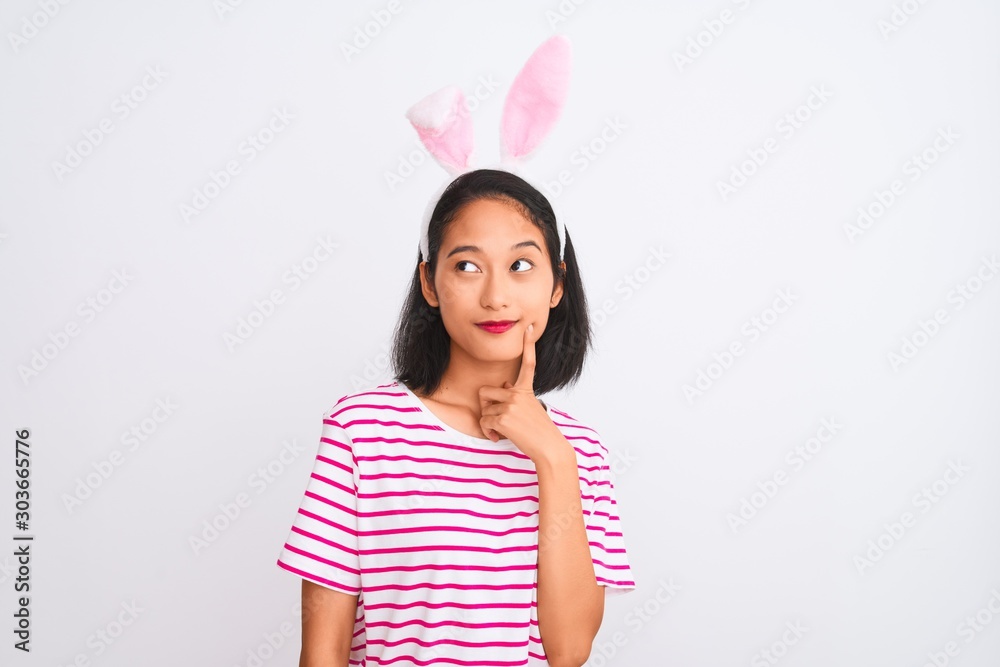 Young beautiful chinese woman wearing banny ears standing over isolated white background serious face thinking about question, very confused idea Young beautiful chinese woman wearing banny ears standing over isolated white background serious face thinking about question, very confused idea