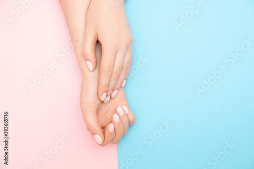 Beautiful female hands with stylish nail manicure gel polish on pink and blue background, top view. Skin care concept